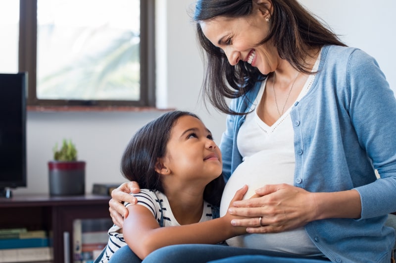 pregnant woman smiling at daughter holding belly