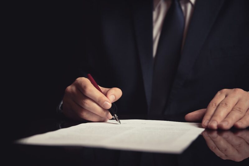 Man in business attire signing a piece of paper on a desk